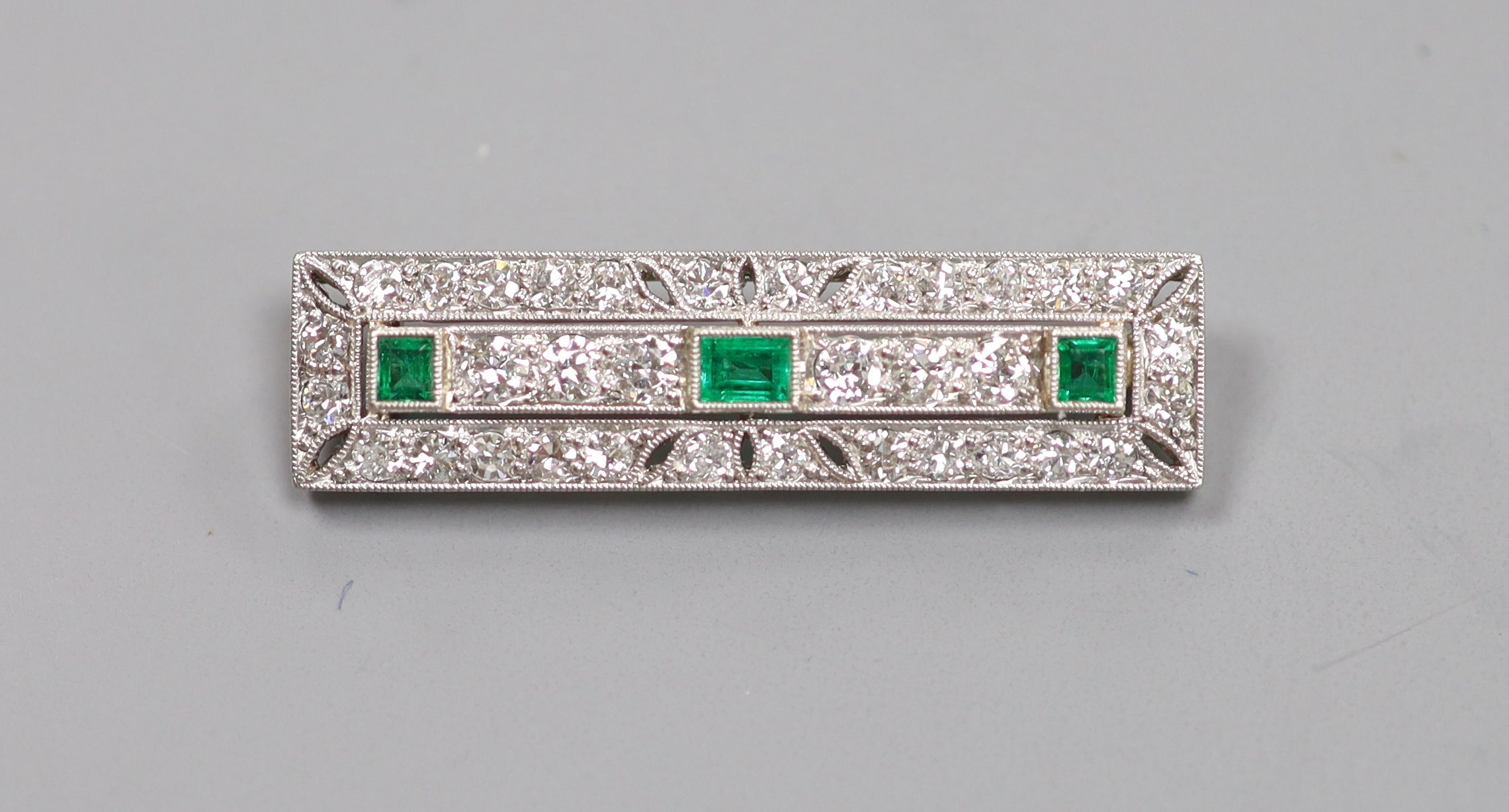 An Art Deco pierced 18ct and plat, emerald and diamond millegrain set rectangular brooch